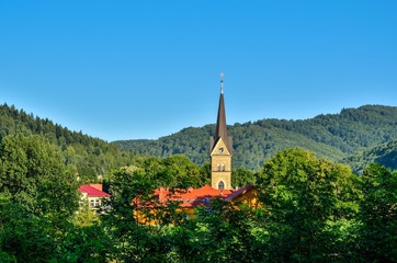 Mountain summer landscape. Church tower in the countryside on a background of beautiful green hills.