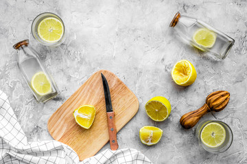 Obraz na płótnie Canvas Prepare refreshing beverage lemonade. Lemons, juicer, bottle, knife, cutting board on grey stone background top view copyspace