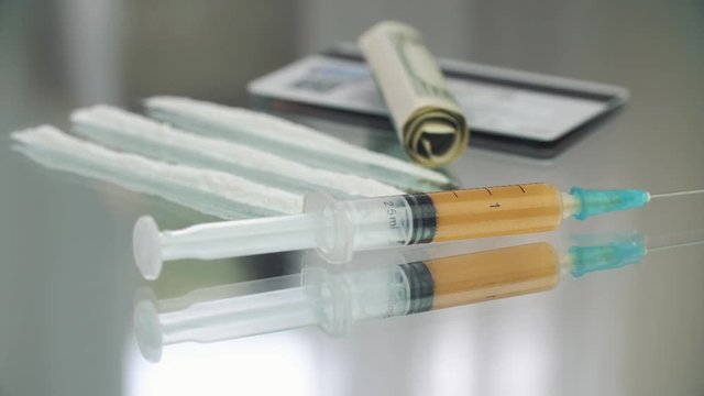 Cocaine powder, medicine syringe on the glass table 