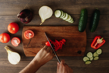 The chef cuts fresh and tasty vegetables for cooking. Hands close-up. View from above. Wooden brown background. Beautiful food still life.