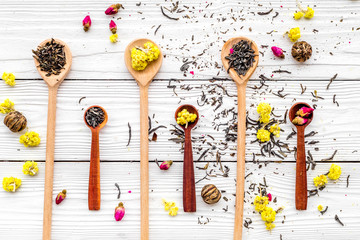 Aromatic tea. Wooden spoons with dried tea leaves, flowers and spices on white wooden background top view