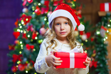 Little girl sitting by the tree holding a Christmas gift In the 