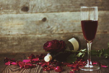 glass of wine and a rose and rose petals on wooden background