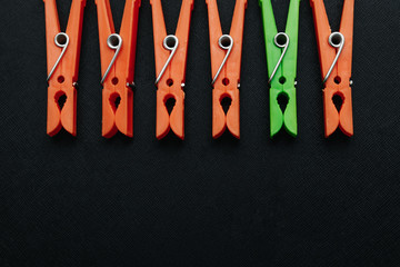 One green, linen clothespin in a row of orange, linen clothespins on a black background. Creative image, background. The concept is not like everyone else, an outcast, another.