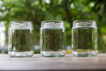 Fototapeta na wymiar Three empty round shape glass canisters on wooden desk with nature background