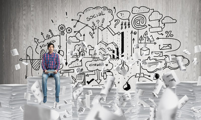 Attractive man sitting on pile of paper documents.