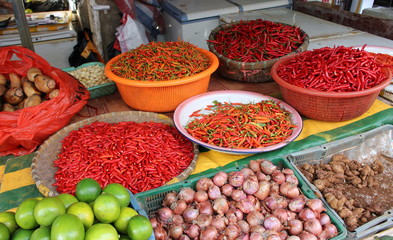 A wide variety of fresh red chili peppers of local varieties on the street market in China. In the foreground lie the fruits of lime, onions and ginger. There is no merchant behind the counter.