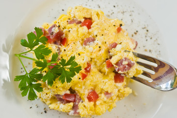 Salami and egg tart / Salami and egg tart in a polenta crust with chopped tomato and fresh ground pepper and a sprig of parsley on a round, white plate with a fork in the meal, paleo diet