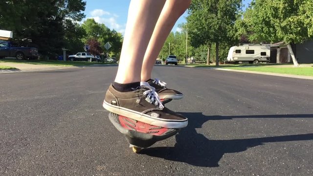 Girl on skateboard roller stick approaches camera in slow motion before passing; shot at ground level in angled late afternoon sunlight.  