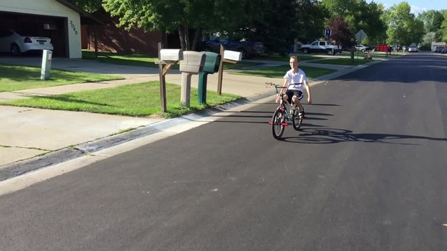 Boy rides bike with no hands in slow motion passing by camera before making a wide turn. 