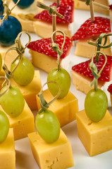 Small sandwiches for the holiday. A plate with many festive snacks for a buffet table. Assortment of canapes from cheese, fruits and berries. Abundance of delicious food.