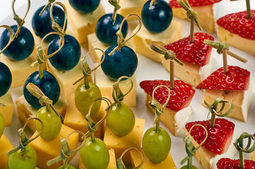 Small sandwiches for the holiday. A plate with many festive snacks for a buffet table. Assortment of canapes from cheese, fruits and berries. Abundance of delicious food.