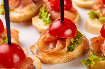 Bruschetta with smoked salmon, greens and small cherry tomatoes. Expensive snack for the festive table. A treat for a wedding, New Year's, Christmas receptions.