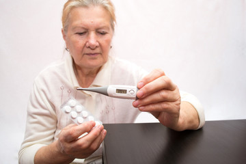 an elderly sick woman is holding a digital thermometer with a high temperature and coughs on a...