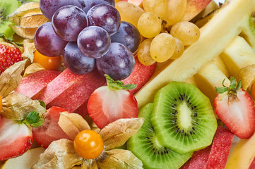 The abundance of exotic fruits and berries on the festive table. Physalis, grapes, strawberry, pear, peach, kiwi, apple, pineapple close-up as background. Food for weight loss.