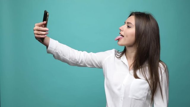 Smiling happy woman in t-shirt making selfie on smartphone over collor background