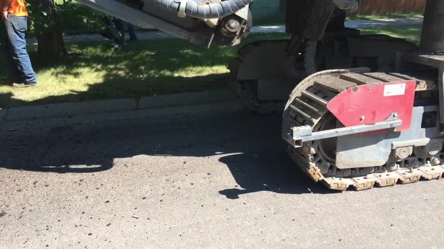 Pavement milling machine rips up road to prepare for new blacktop surface; shot from front where shoot puts materiel into truck back to machine. 