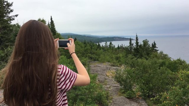 Teenage girl takes pictures of rugged landscape coastline along Lake Superior in northern Minnesota.