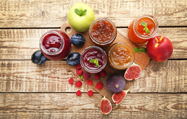 Glass jars with different kinds of jam and berries on wooden table