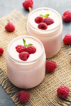 Raspberries yogurt in jars on wooden table