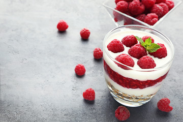 Dessert with raspberries and granola in glasses on grey wooden table