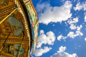 Old Parisian carousel against blue sky with clouds in sunny day.