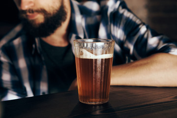 A young guy with a beard drinks beer in a bar