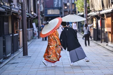 Zelfklevend Fotobehang traditional japanese costumes kimono worn by bride and groom with original umbrellas taking photo shots on the marriage day in kyoto japan © gilad