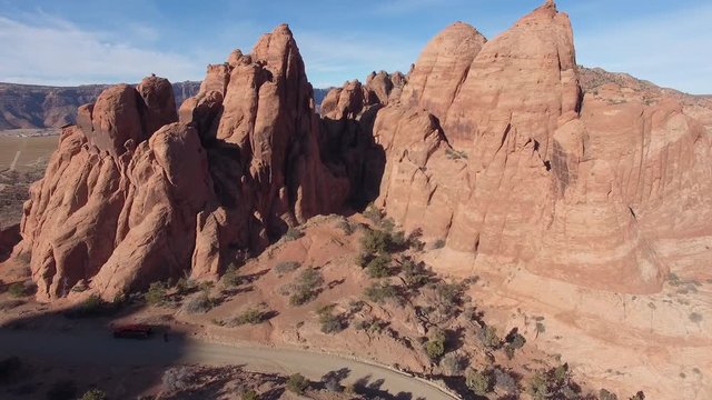 Flying through red rock desert terrain past cliff  in Moab Utah viewing dirt road and revealing small lake and landscapes in the valley.