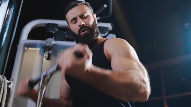 Strong man is pumping muscles at the gym, strength exercises on simulators, athlete at fitness club, caucasian man with beard