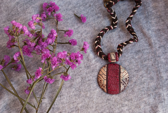 Background with pink flowers and african pendant. Handmade jewelry of polymer clay.