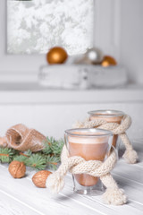 two cappuccino coffee in a glass with a double stack and a scarf are on a wooden white table  by the window