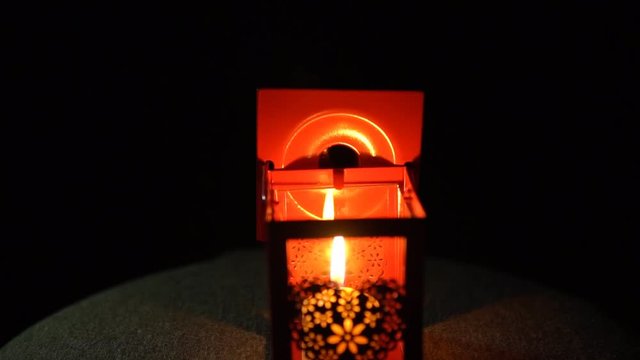 The yellow candle went out in a red metal lantern with a delicate heart on its side on a black background, slow motion.
