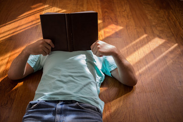 Man reading old hardback book holding in his hands, on the wooden floor at home. Domestic lifestyle. Education concept.