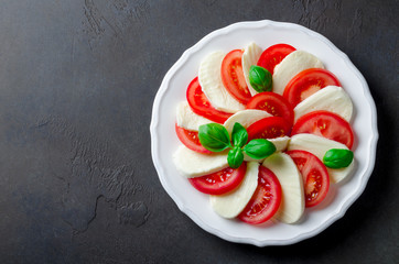 Traditional italian food, caprese, sliced tomatoes and mozzarella on a white plate, dark stone...