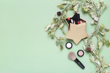 Christmas makeup flat lay on green background surrounded by holly plant