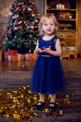 Fototapeta na wymiar girl child blonde in the blue dress standing at the tree and gold confetti
