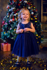 girl child blonde in the blue dress standing at the tree and gold confetti