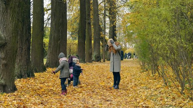 Children playing with fallen leaves in autumn park. Two kids walking with mom in autumn park