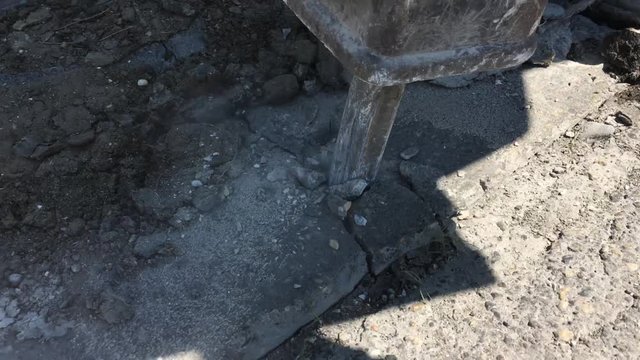 Jackhammer breaking up concrete with small concrete chunks and dust exploding into air.