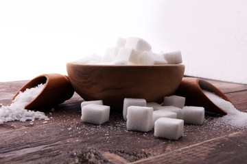 Close up the sugar cubes and cane in wooden spoon on the table.
