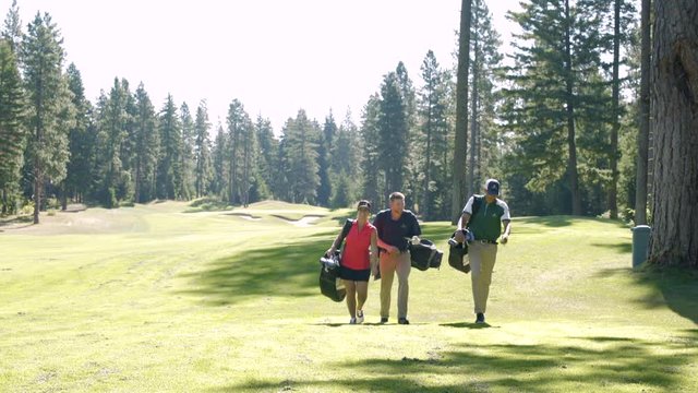 Three people walking on a golf course with sporting equipment