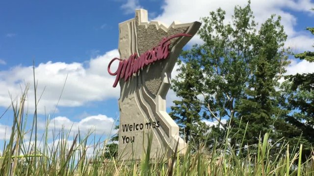 State of Minnesota welcomes you sign shot from ground level, angled and with blue sky and clouds in background.   