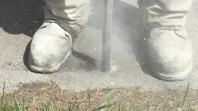 Construction worker drills large hole into concrete in preparation for mud jacking under surface to a level higher.