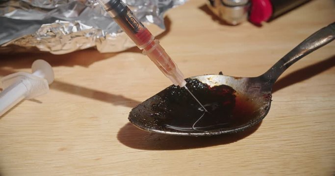 Needle Draws Heroin Drug Off Spoon Close Up. a close up view of a burned spoon with foil and lighter with a syringe sucking up the drug liquid on the spoon