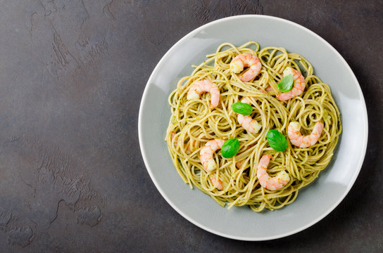 Spaghetti with fried prawns and pesto sauce in a gray plate, dar