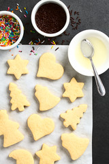 Weihnachtliche Butterplätzchen auf Backpapier mit Zuckerguss und Streuseln an der Seite