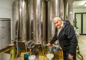 old man opens tap of storage silo of olive oil