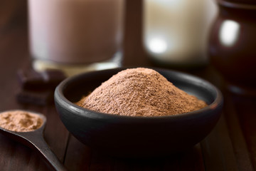 Cocoa or chocolate drink powder in rustic bowl, chocolate drink and milk in the back, photographed with natural light (Selective Focus, Focus one third into the cocoa)