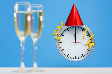 series of a Cute simple clock wearing a Red Party Hat on New Years Eve at Midnight, on bright blue background and two blurred champagne glasses